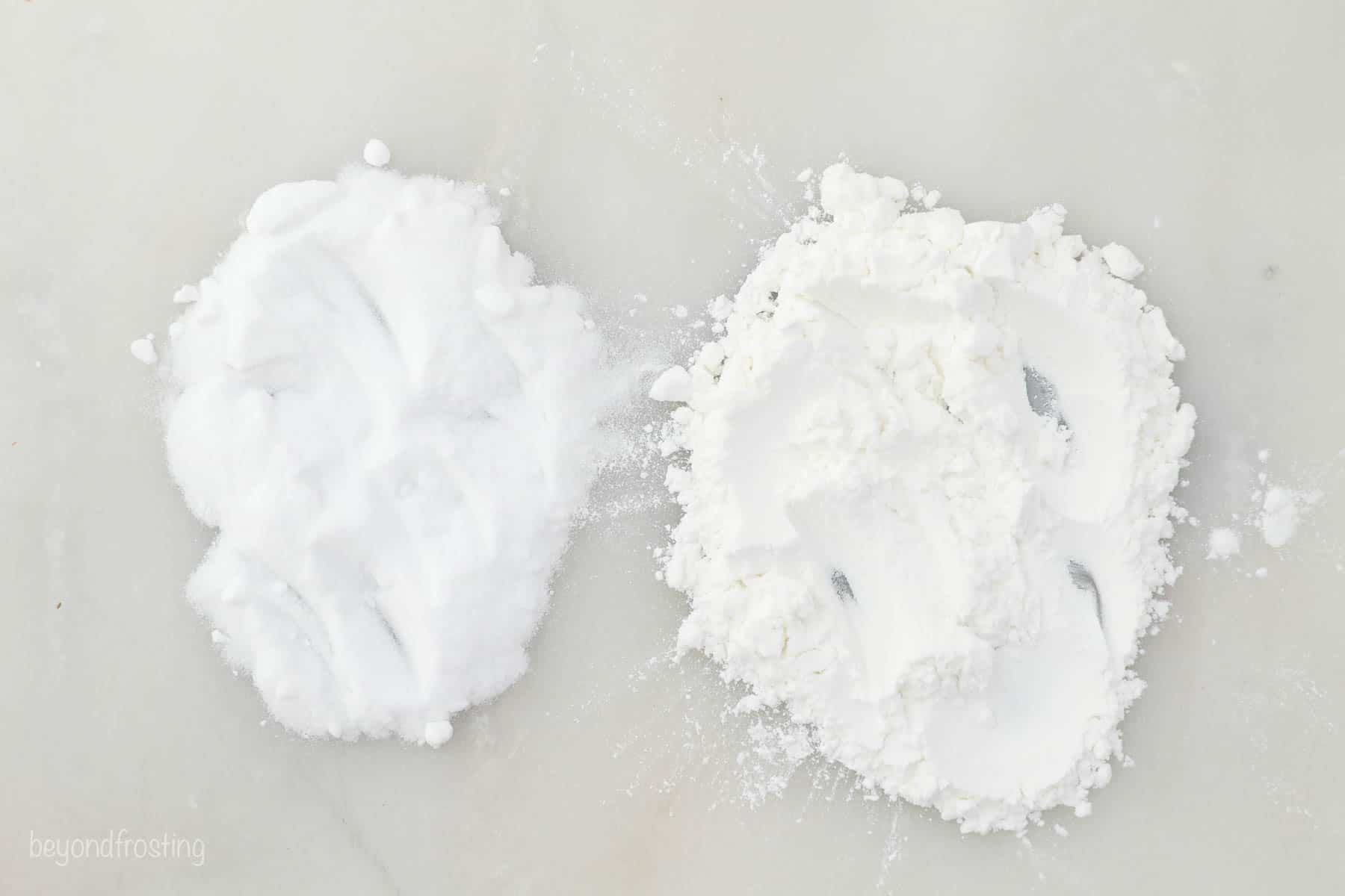 A pile of baking soda on a white surface beside a pile of baking powder