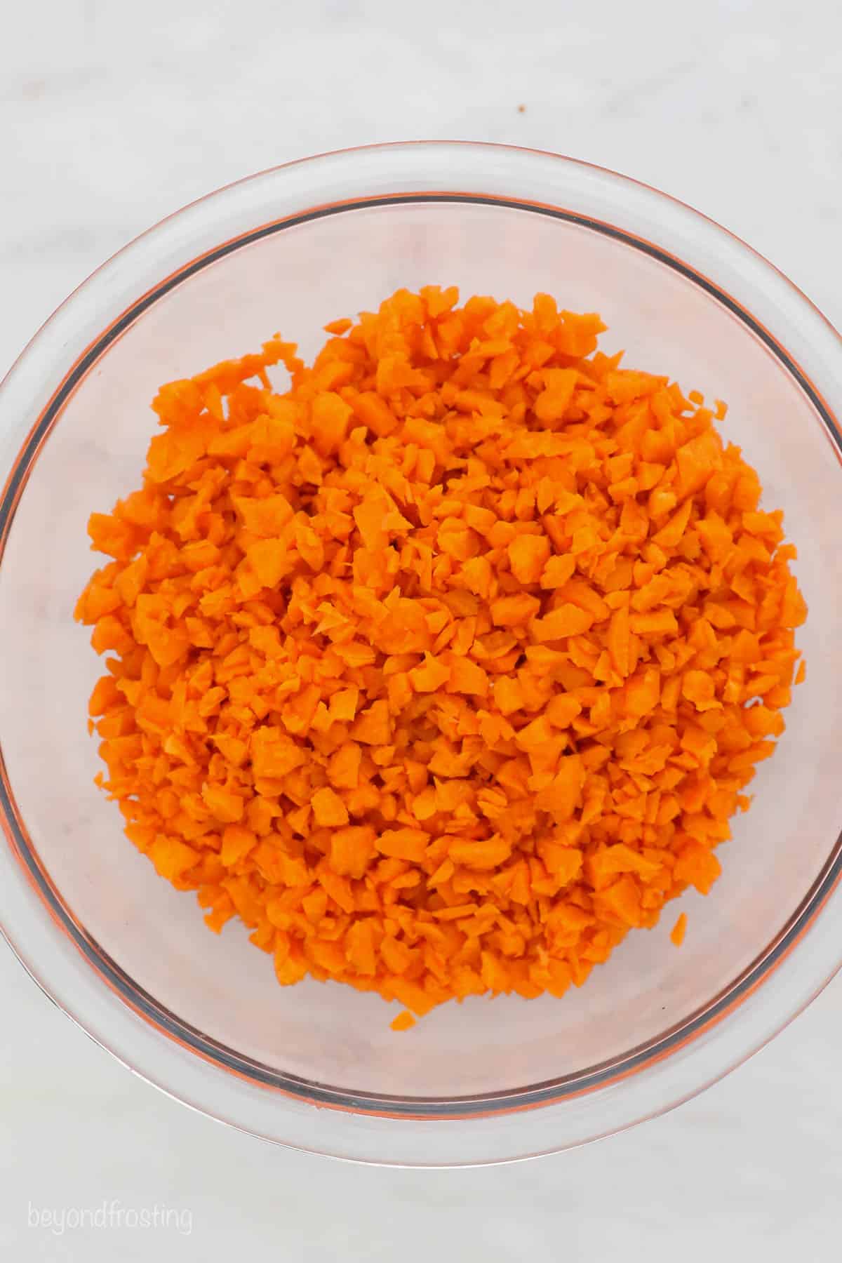 A glass mixing bowl filled with shredded carrots on a kitchen countertop