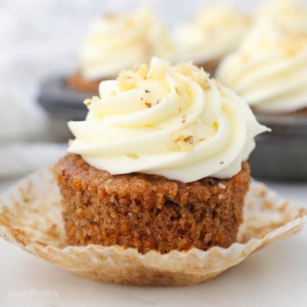 A close-up shot of a classic carrot cake cupcake topped with a swirl of whipped cream cheese frosting
