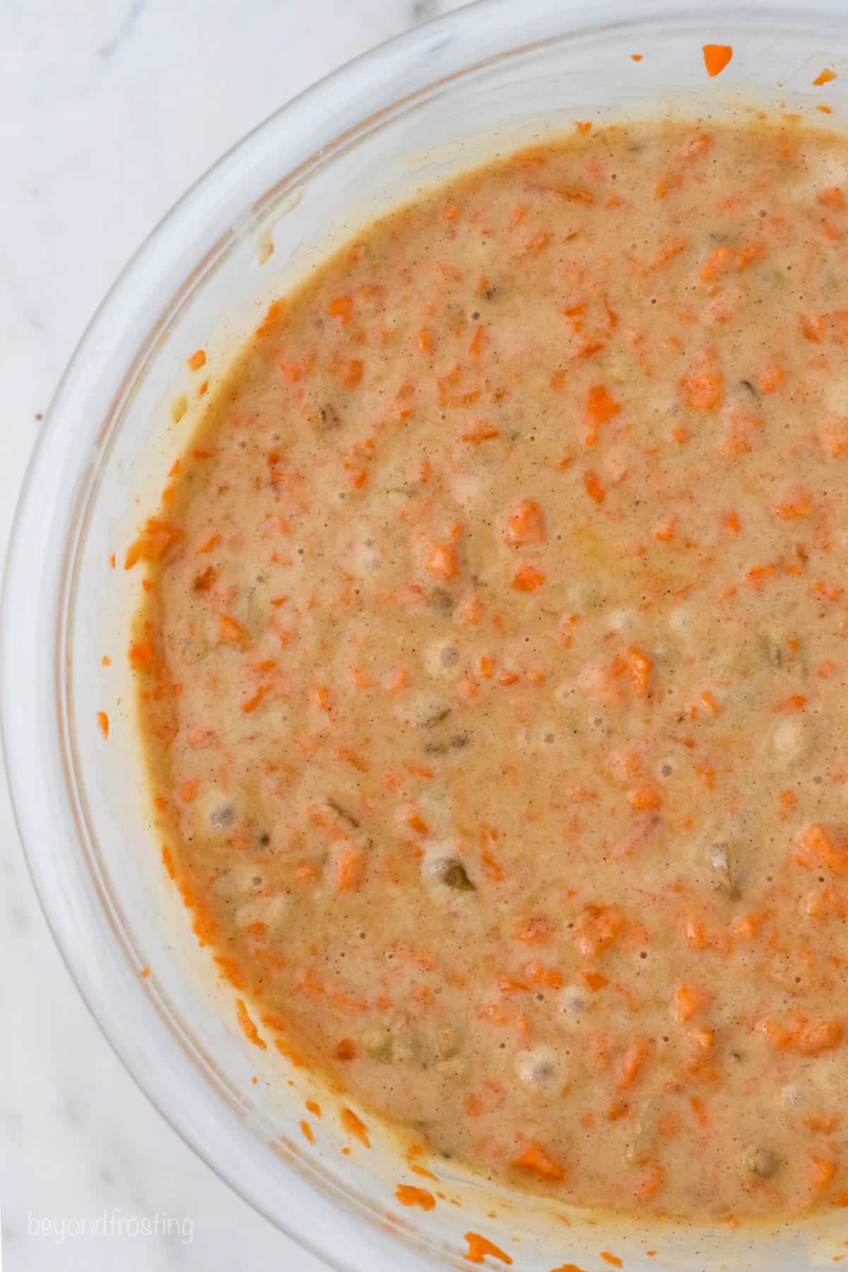 A close up of carrot cake batter in a glass mixing bowl
