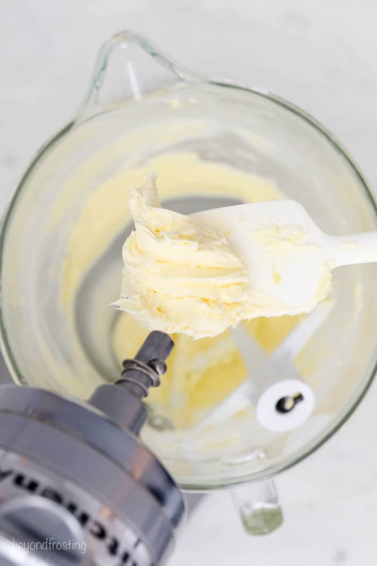 a white spatula with creamed butter handing over a stand mixer