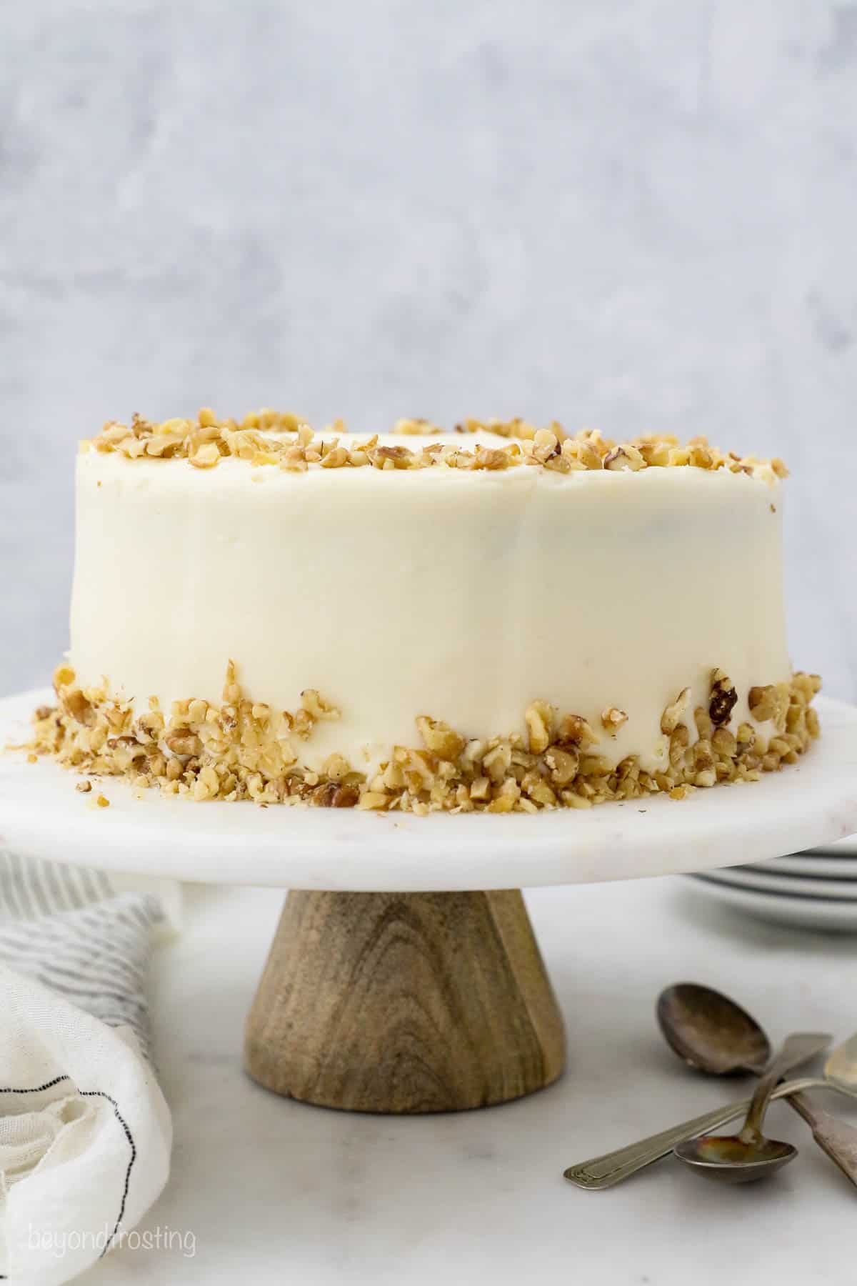 A finished Carrot Cake garnish with chopped nuts on a marble cake stand