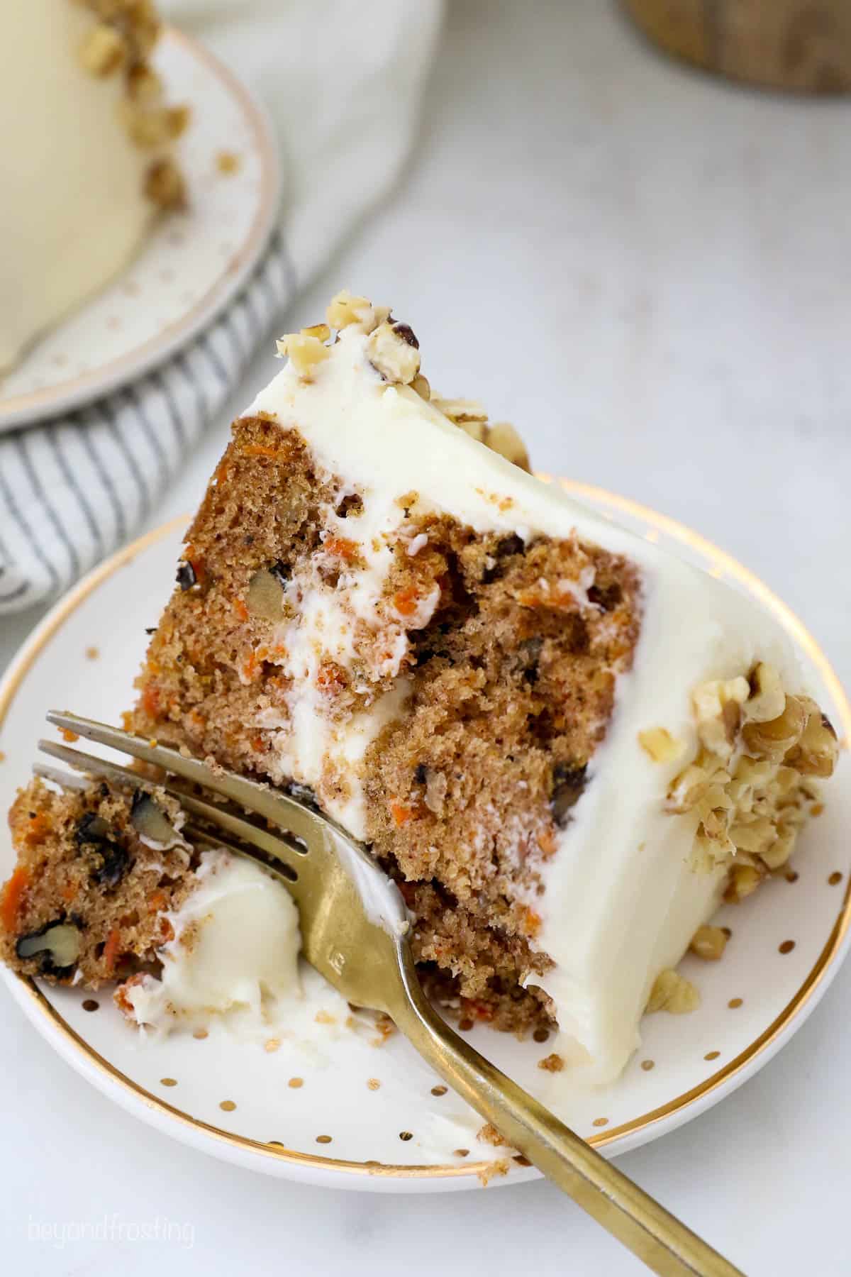 My grandma's homemade carrot cake recipe is warmly spiced with the perfect ratio of moist cake to rich cream cheese frosting. Easy to make! A slice of carrot cake on a plate with a bite missing and a gold fork laying across the plate