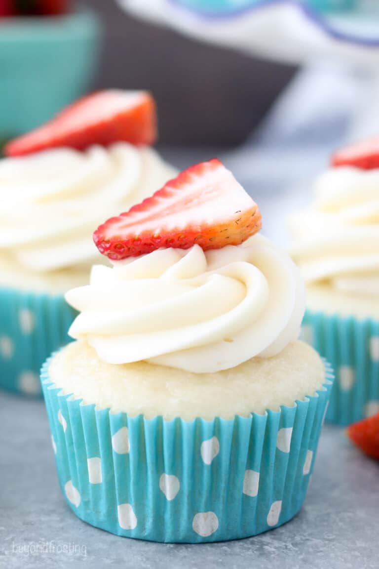 Three cupcakes frosted with cream cheese frosting and a strawberry on top