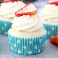 A close up of a frosted cupcake with a strawberry