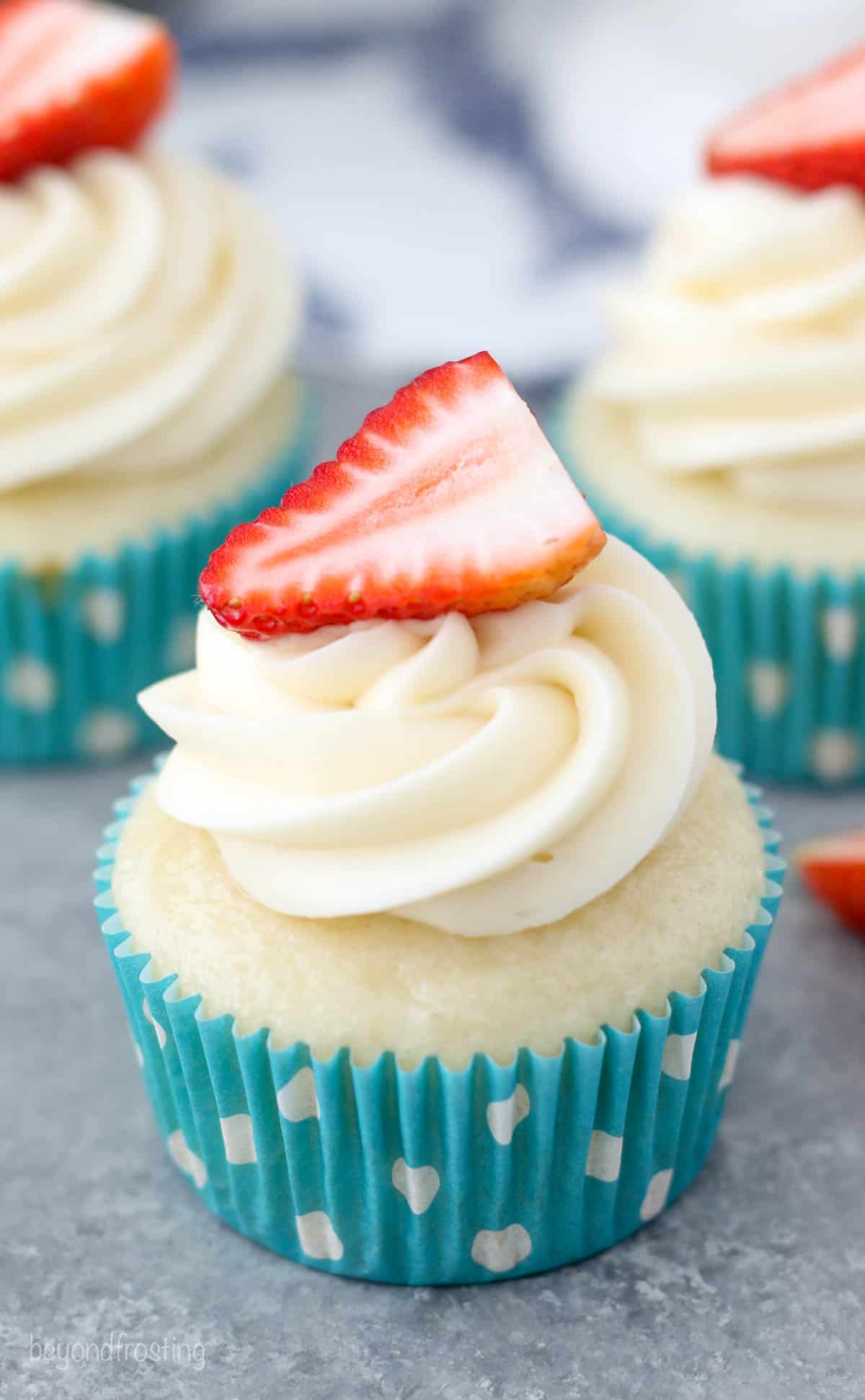 Overhead of a frosted cupcake with cream cheese frosting and a strawberry on top