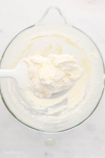 a white spatula floating over a glass mixing bowl with creamed butter