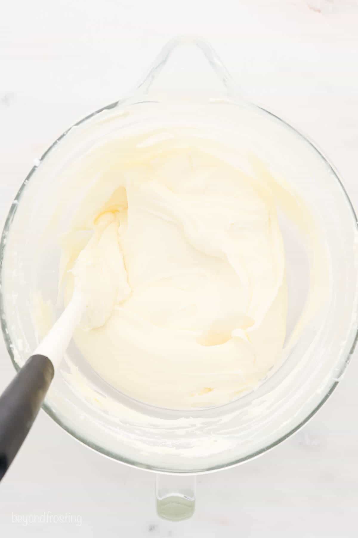 A mixing bowl with cream cheese frosting and a white spatula