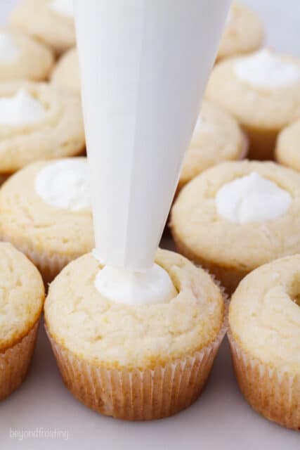vanilla pudding filling being piped into coconut cupcakes