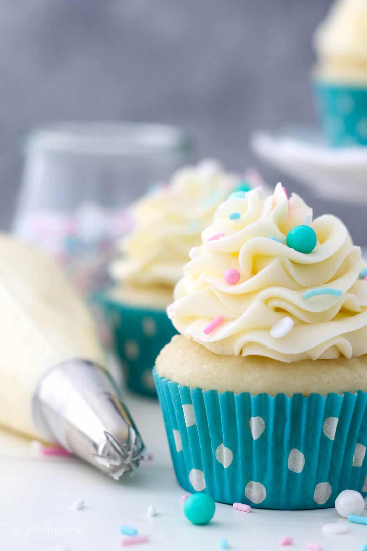 A close up of a frosted vanilla cupcake in a teal polka dot liner