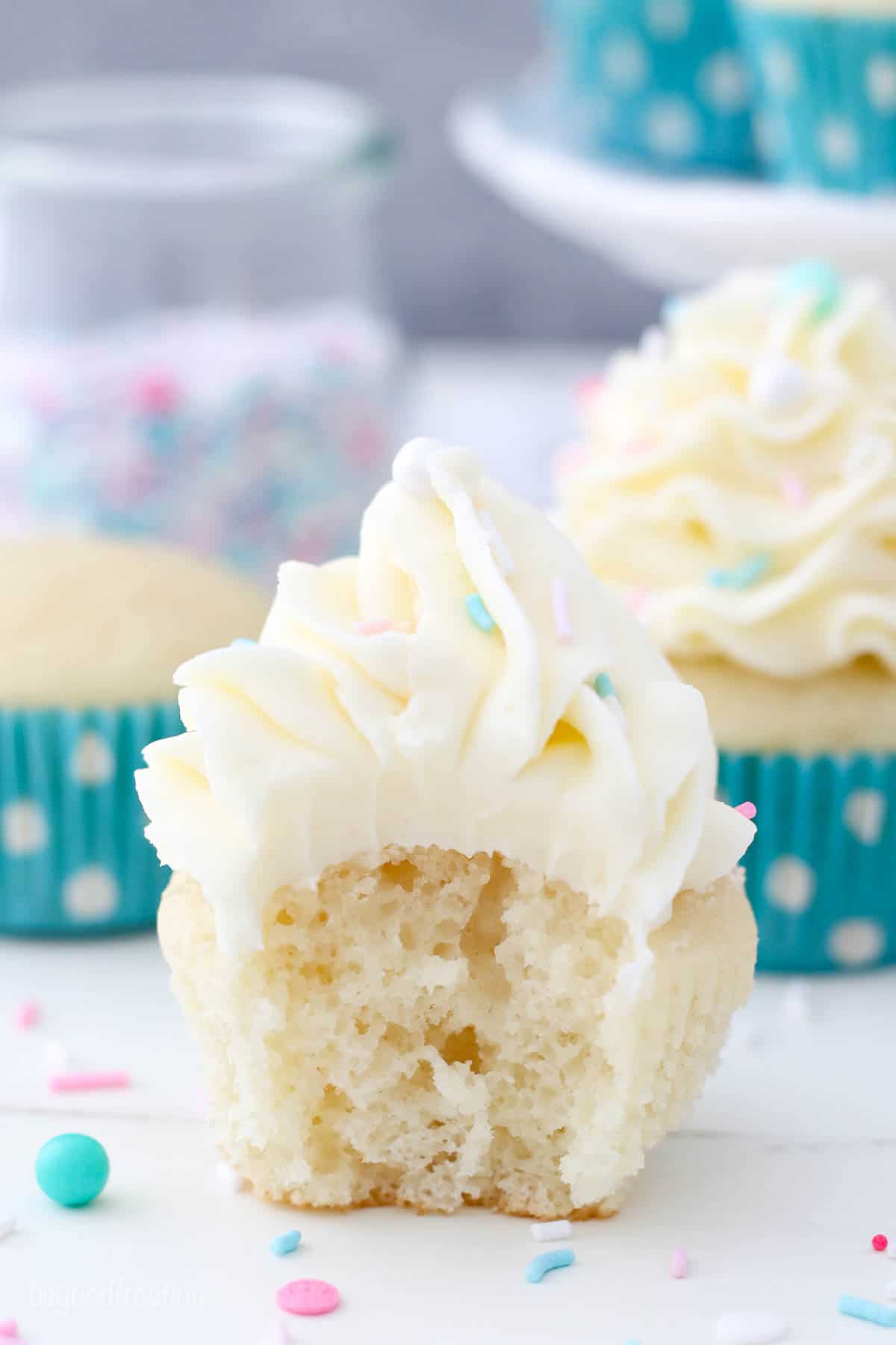 A white cupcake with a bite missing frosted with vanilla buttercream