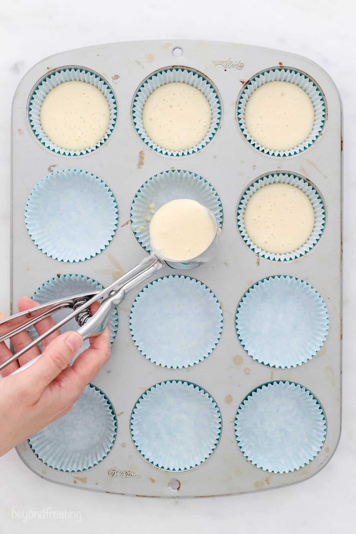 a large cookie scoop filling a cupcake pan with batter
