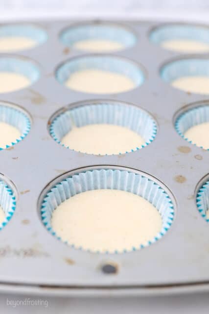 A cupcake pan with teal liners filled with vanilla cupcake batter
