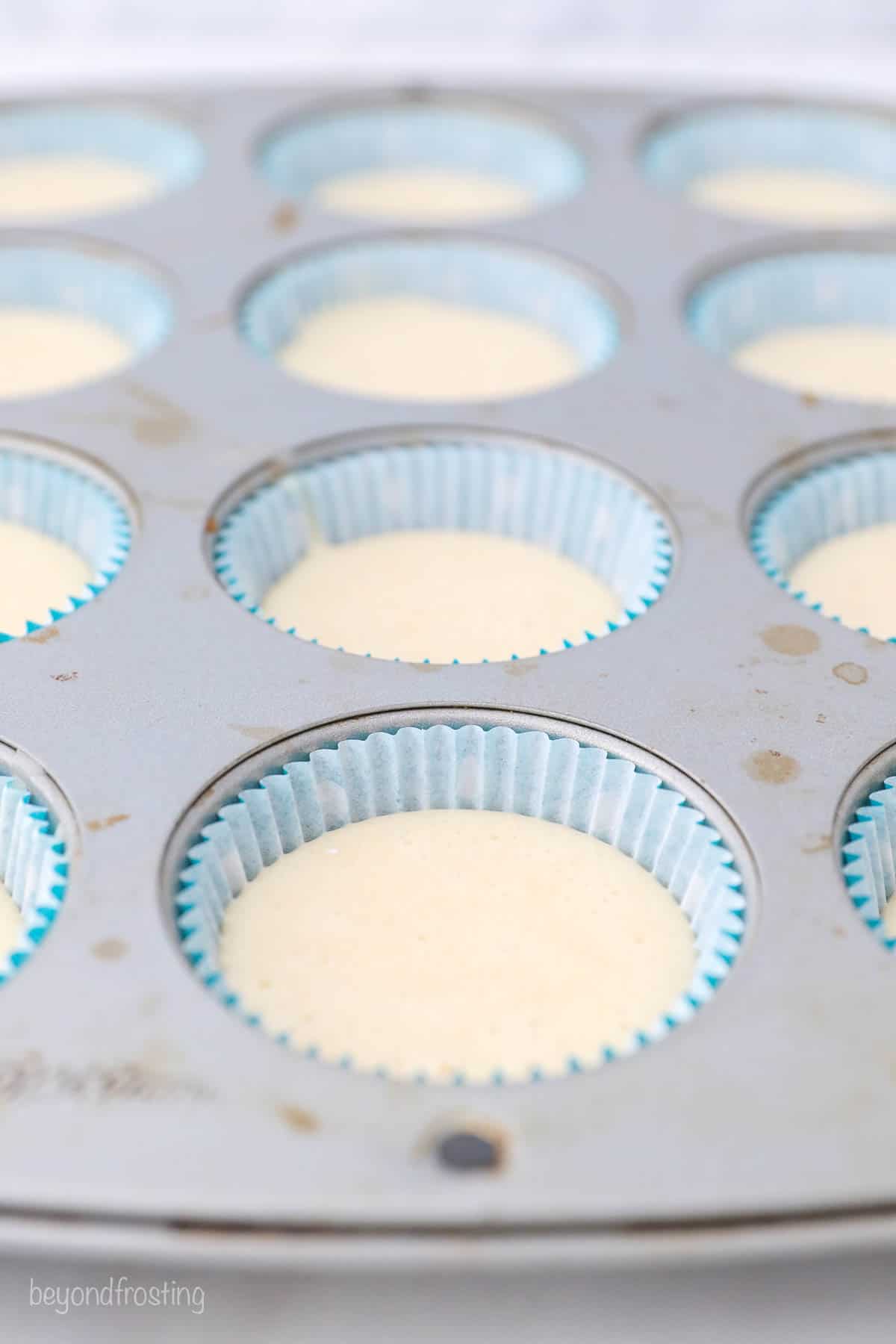 A cupcake pan with teal liners filled with vanilla cupcake batter