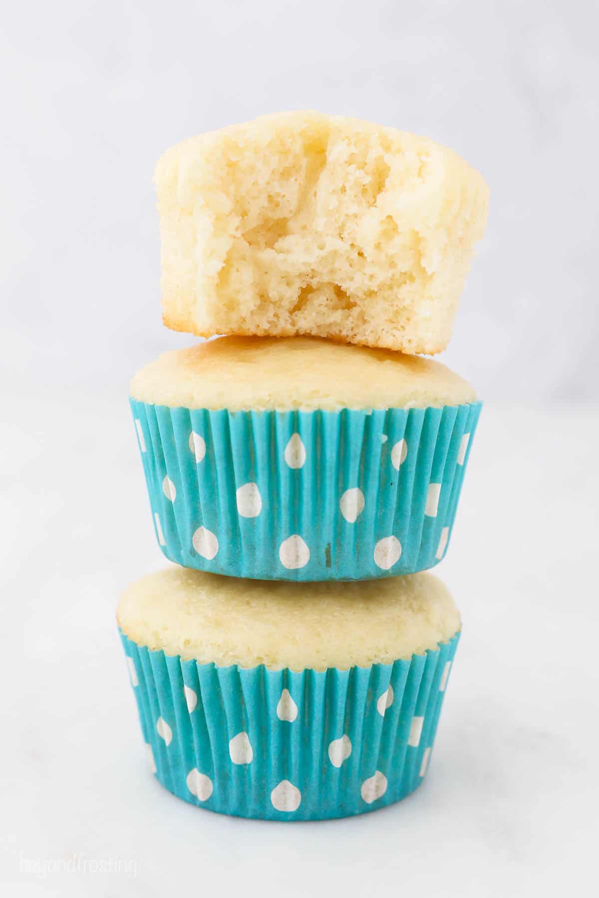 Three stacked vanilla cupcakes, the one on top has a bite missing