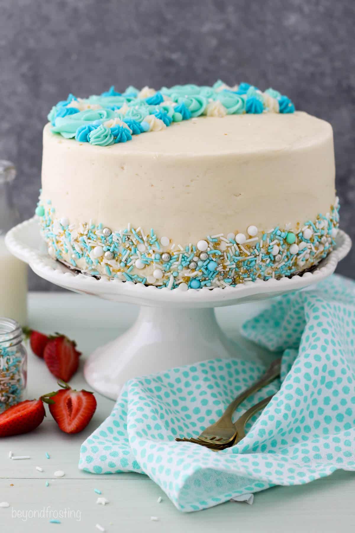 A vanilla cake with blue sprinkles on a white cake stand
