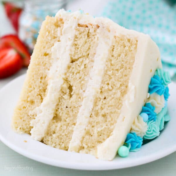 A close up of a slice of a 3 layer vanilla cake on a white plate
