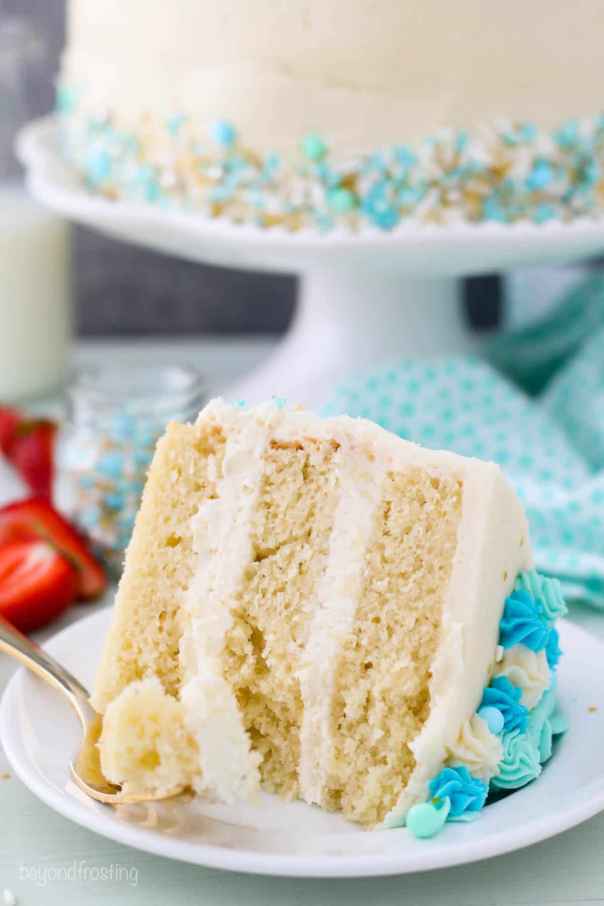A close up of a slice of a 3 layer vanilla cake with a couple bites missing