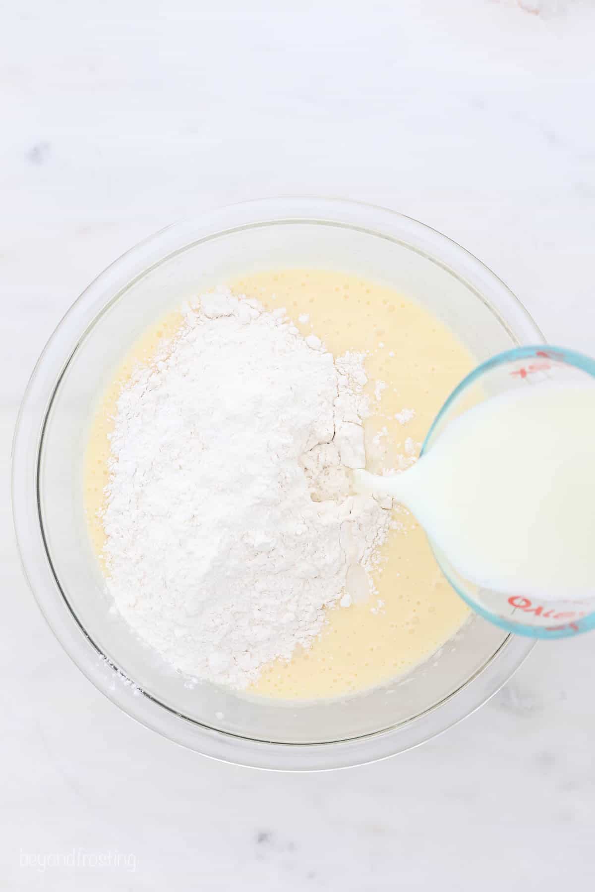 Flour and milk being pouring into a clear glass mixing bowl