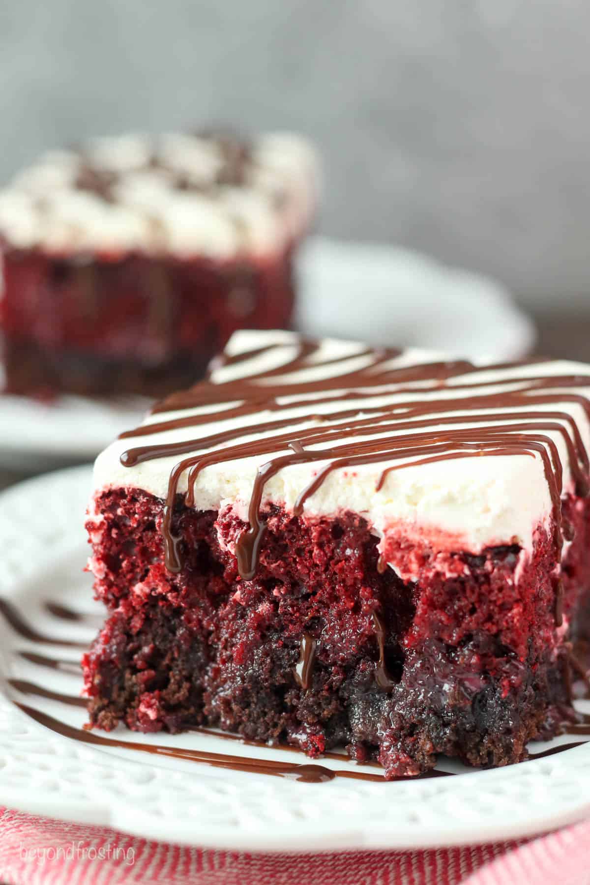 A piece of red velvet fudge poke cake on a plate on top of a wicker placemat