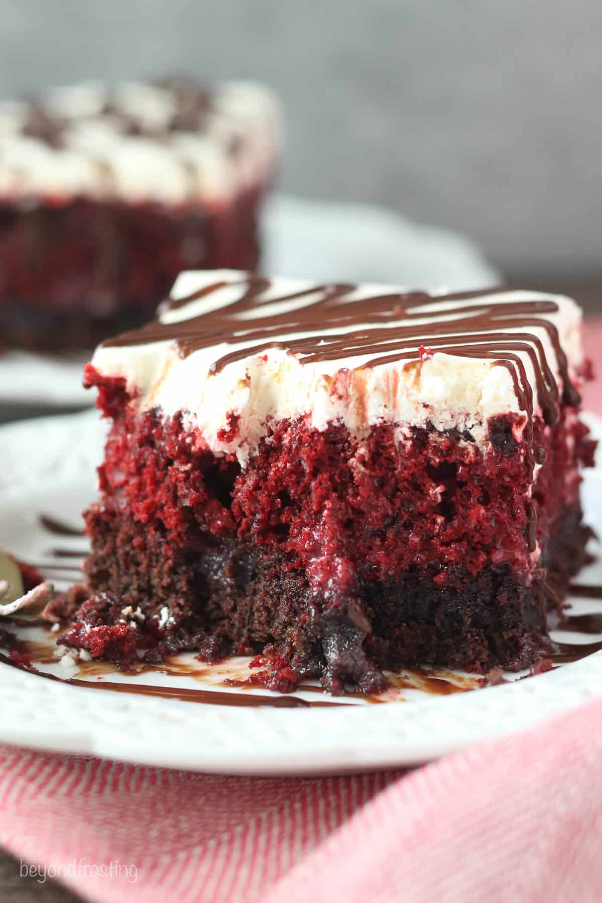 A large piece of red velvet poke cake on a dessert plate with multiple bites gone