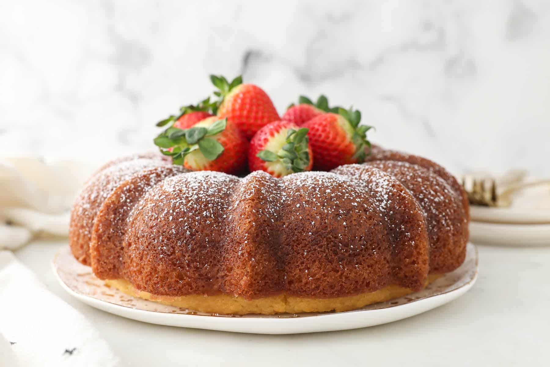 A spiced rum bundt cake topped with a dusting of powdered sugar and a pile of fresh strawberries