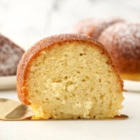 A slice of spiced rum cake on a golden dessert spatula with the rest of the cake in the background