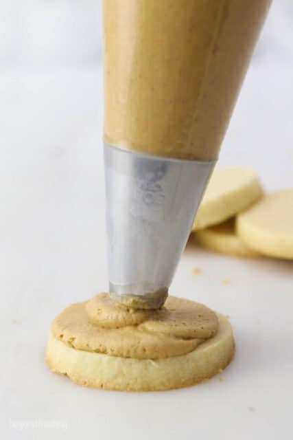 A piping bag filled with peanut butter piping onto a cookie