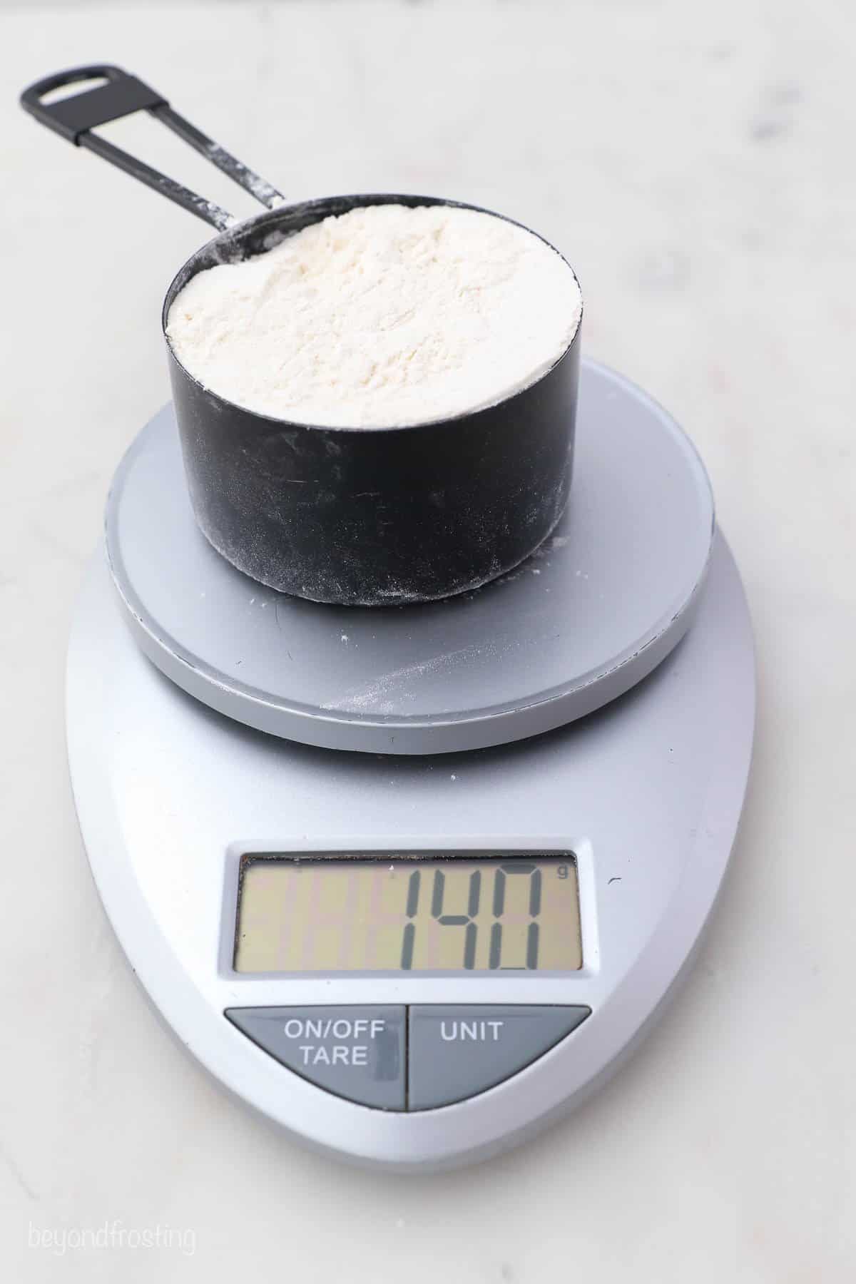 A cup of flour on a kitchen scale weighing 140 grams
