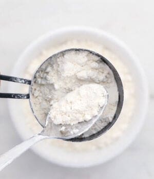 A standard-size spoon scooping some fluffed-up flour into a measuring cup