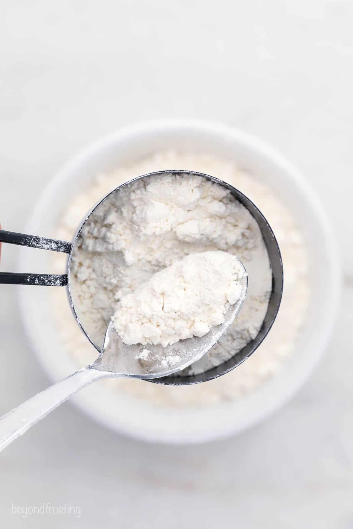 A standard-size spoon scooping some fluffed-up flour into a measuring cup