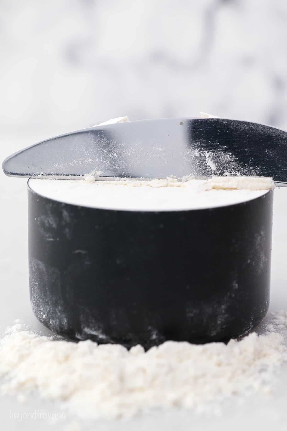 A butter knife leveling off a cup of spooned-in flour at the top