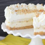 A close-up shot of a banana pudding cheesecake on a large platter with two slices missing