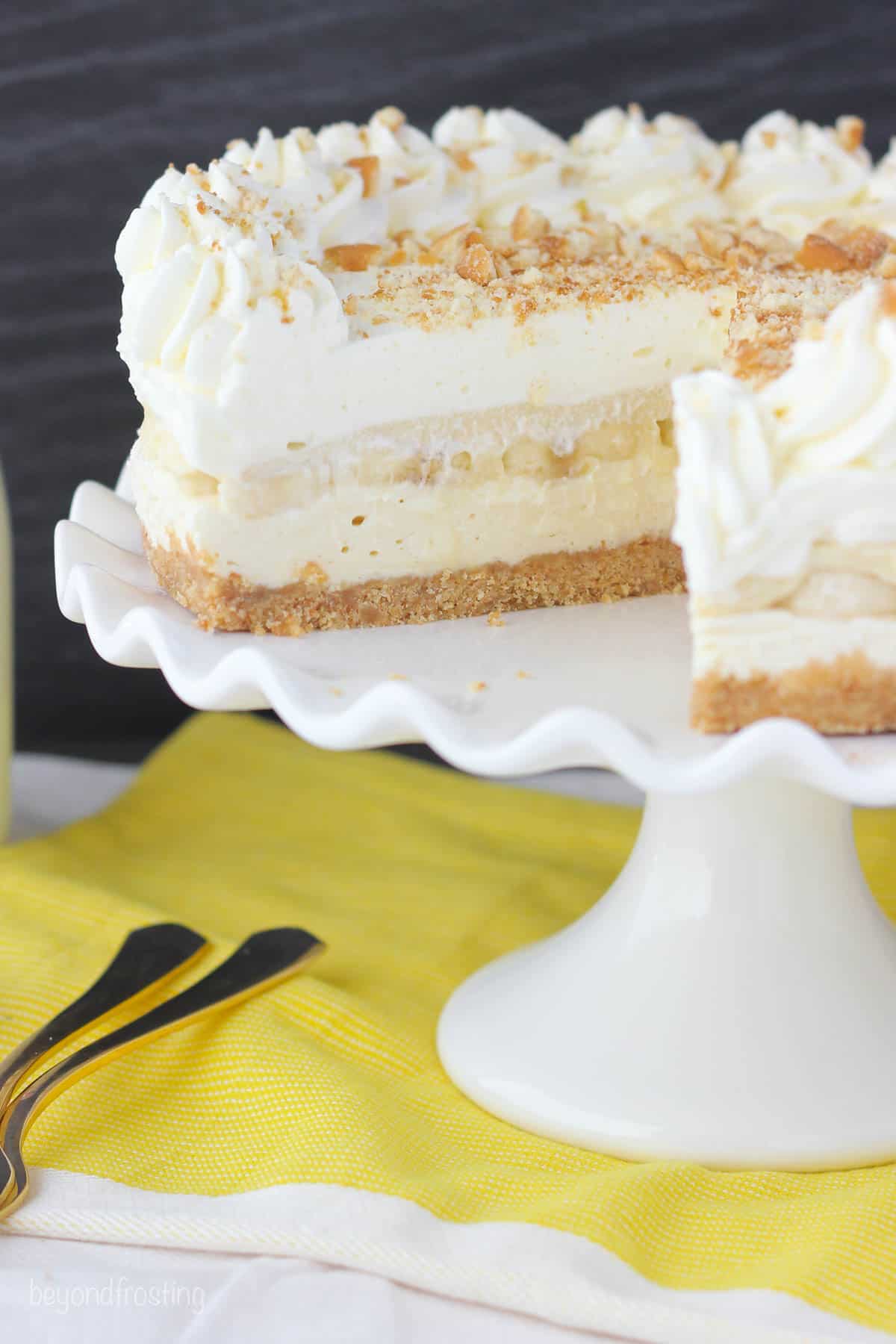 A banana layer cake on a tall cake stand with a yellow dishtowel underneath it