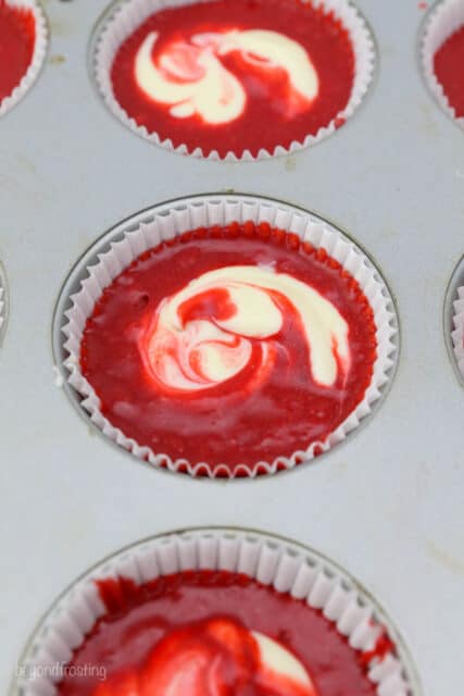 A cupcake pan filled with red velvet cake batter showing the cheesecake filling swirl