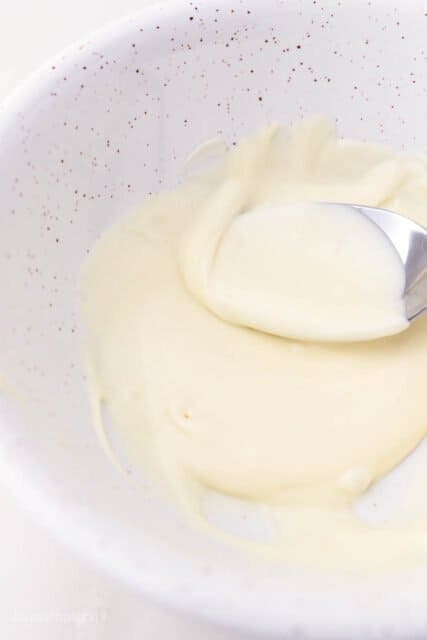 A spoon stirring a bowl of melted white chocolate