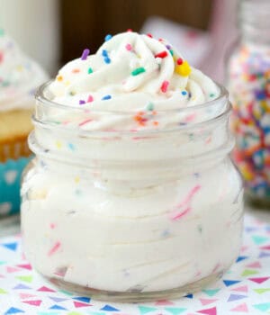 A glass jar of cake batter whipped cream and sprinkles