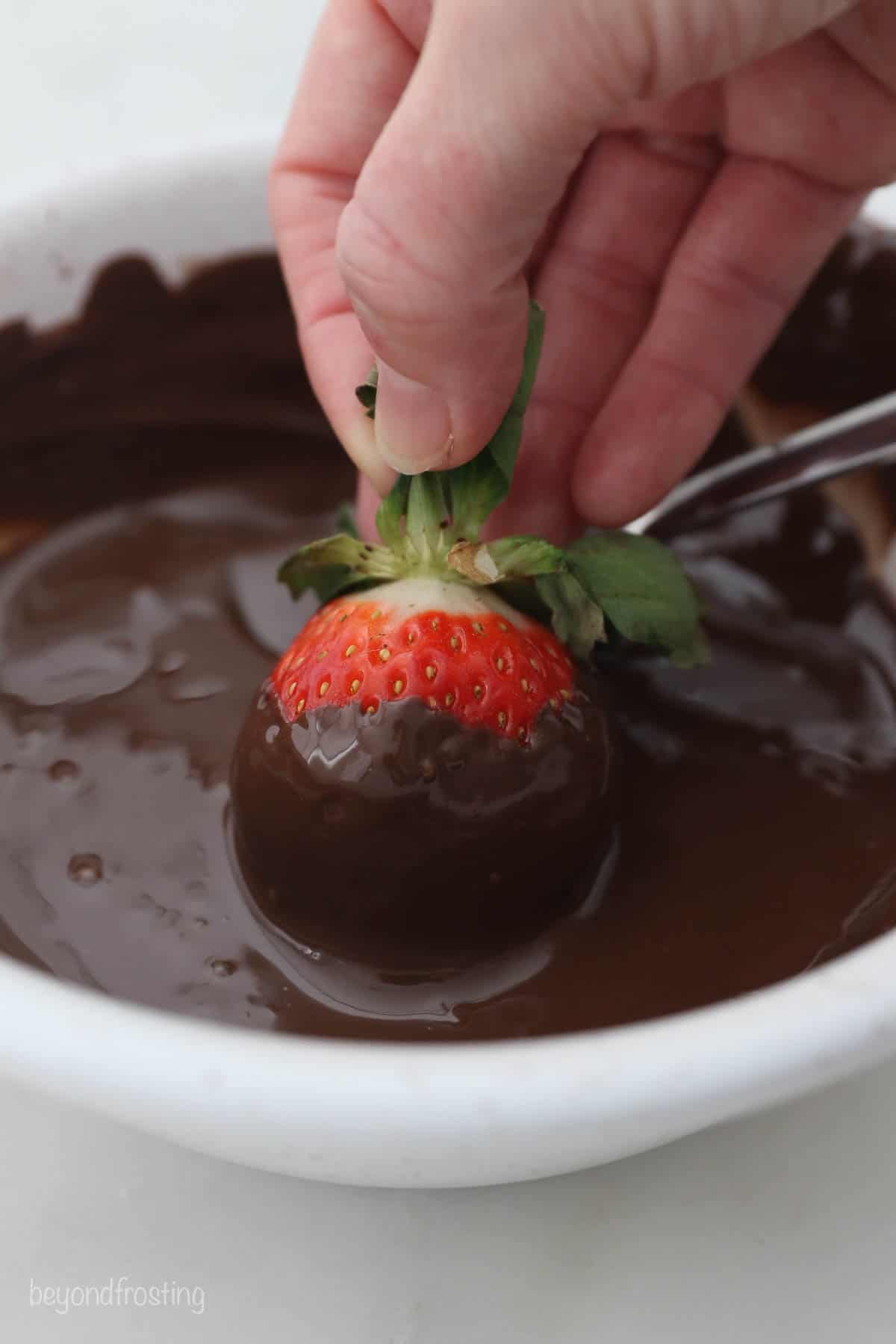 A hand dipping a strawberry into a bowl of melted chocolate