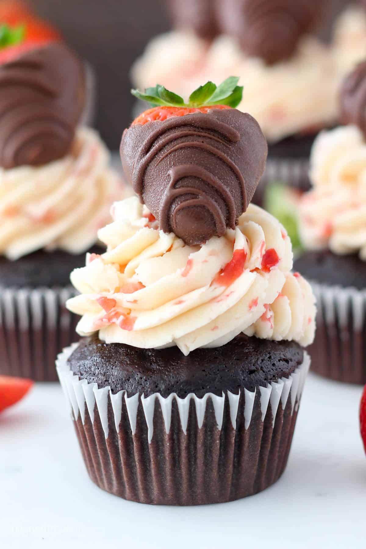 Three chocolate cupcakes covered with fresh strawberry buttercream and they're topped with a chocolate covered strawberry.