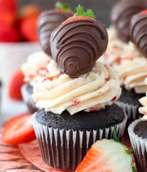A close up of a chocolate covered strawberry cupcake on a pink glass cake plate.