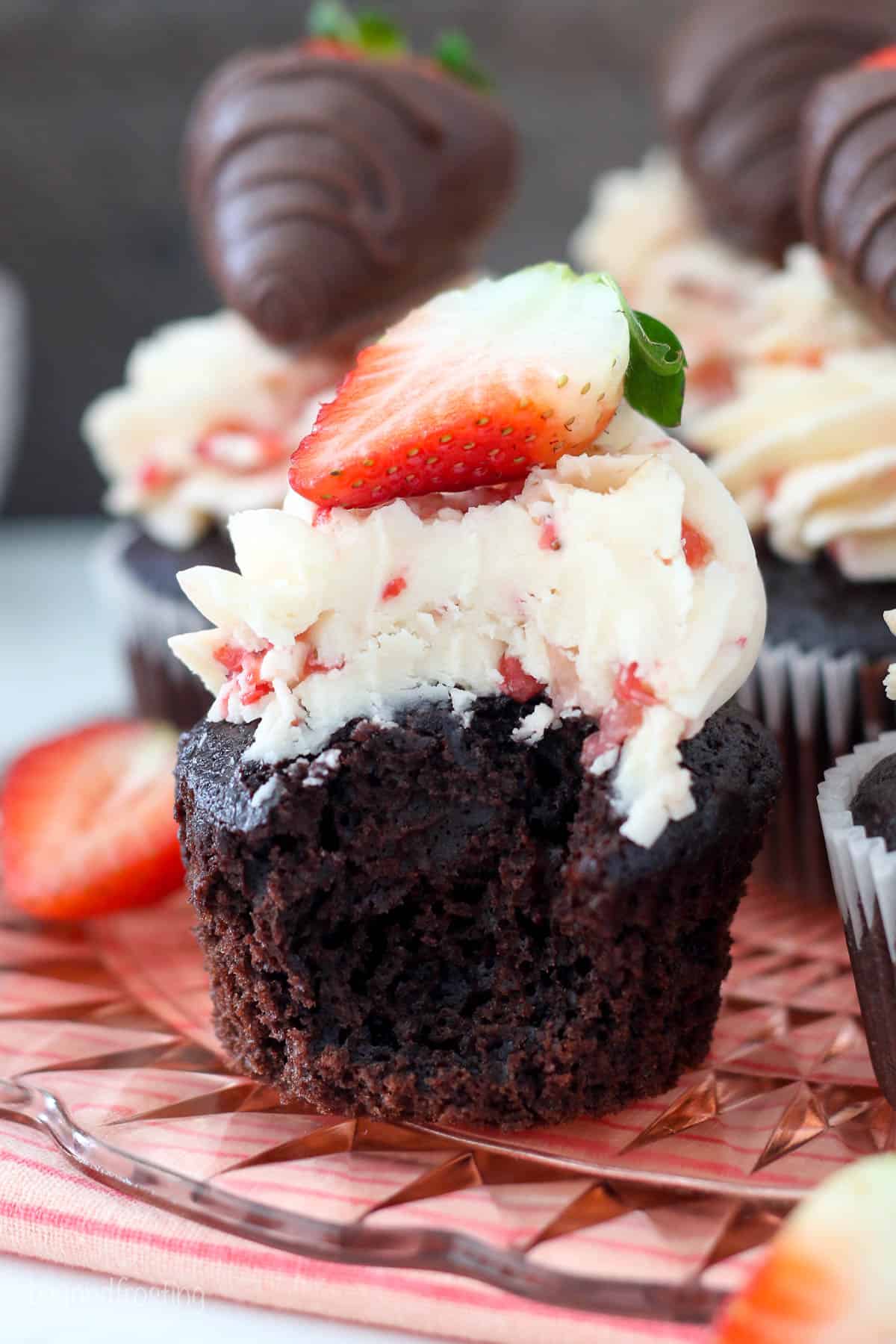 A chocolate cupcake with strawberry frosting has a big bite taken out of it showing the inside of the cupcake and frosting.
