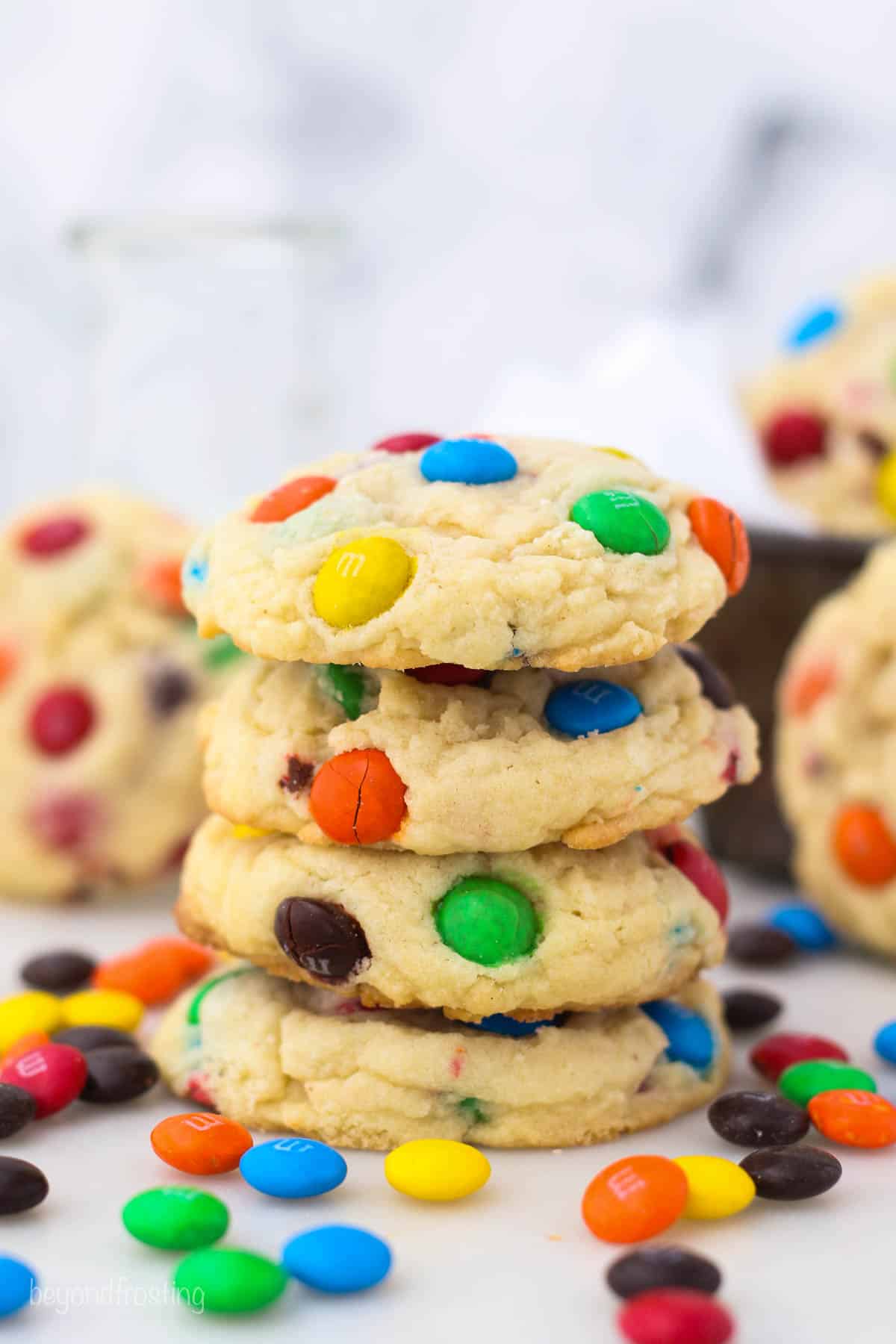 A stack of four M&M cookies surrounded by M&M candies on a countertop.