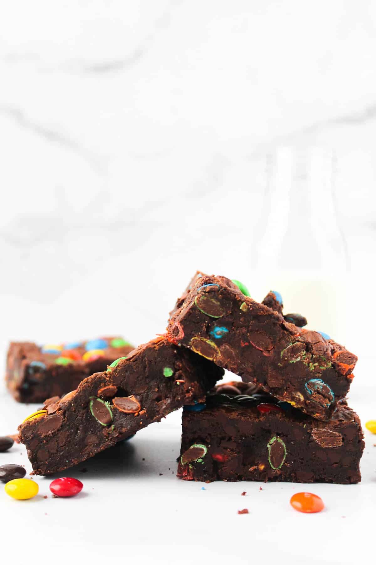 Side view of three M&M brownies stacked in a pile on white countertop.