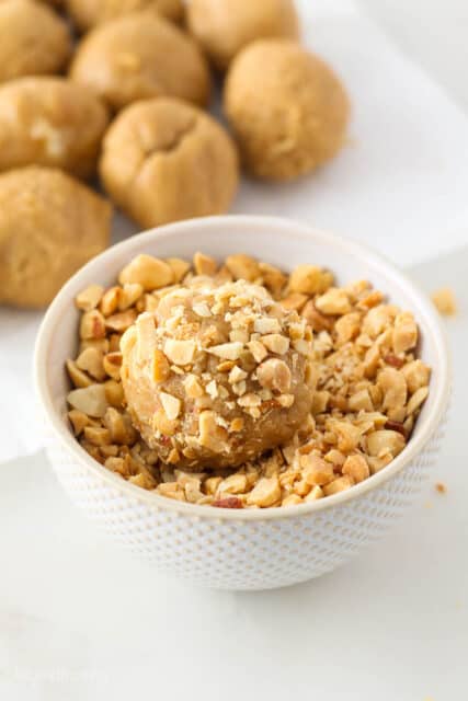 A ball of peanut butter cookie dough being rolled in chopped peanuts