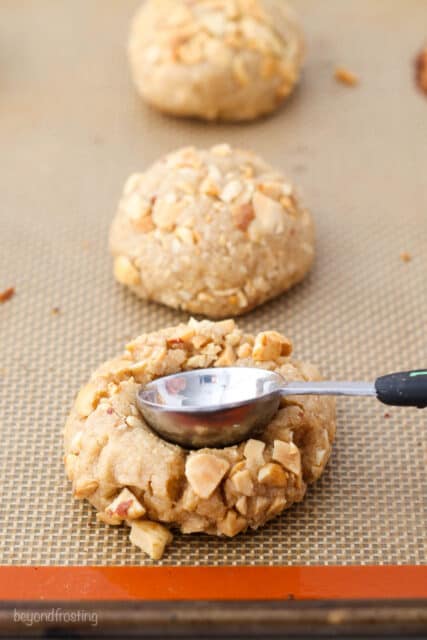 A teaspoon measuring spoon pressing down into a cookie