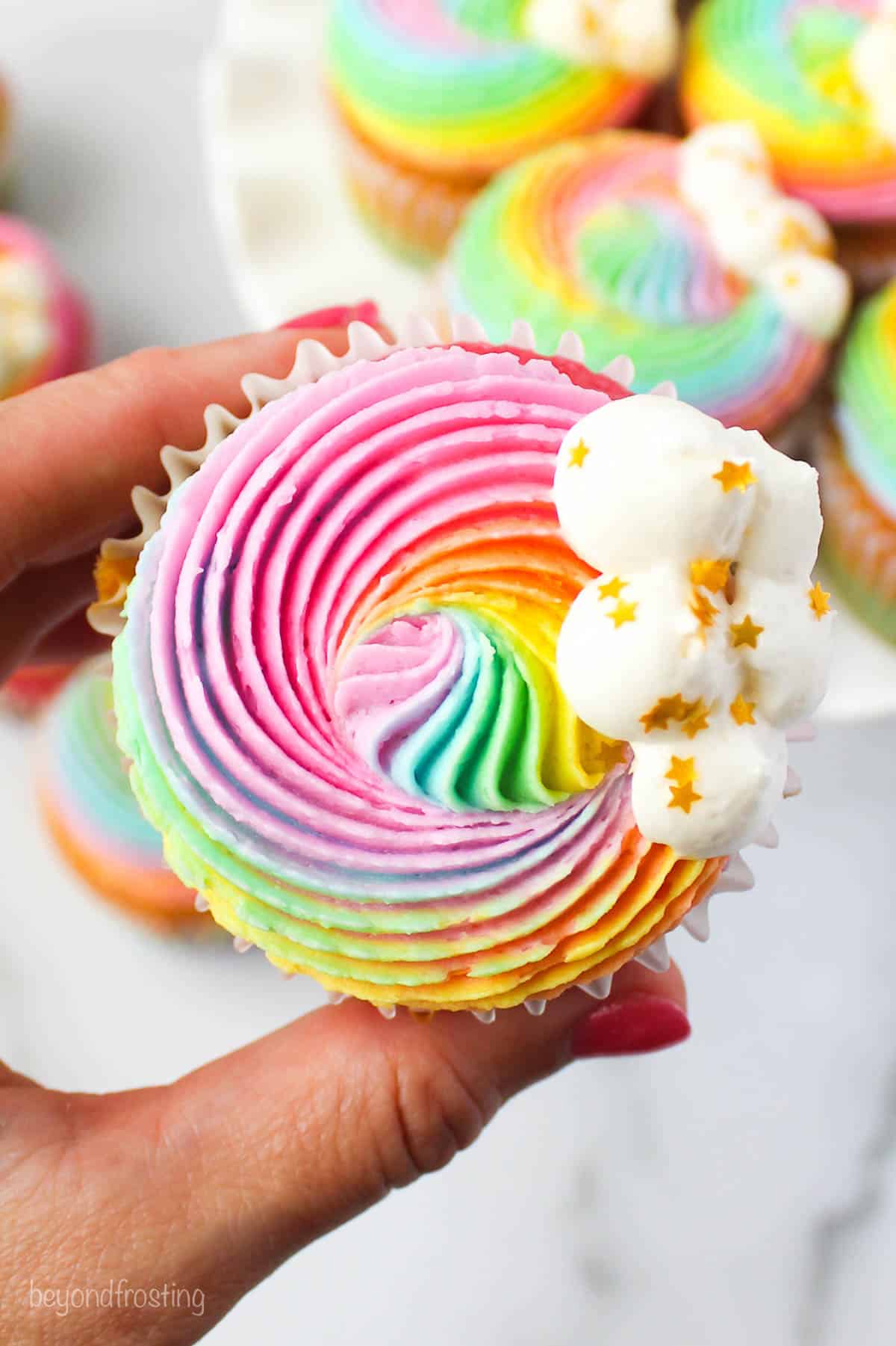 A hand holding a rainbow cupcake