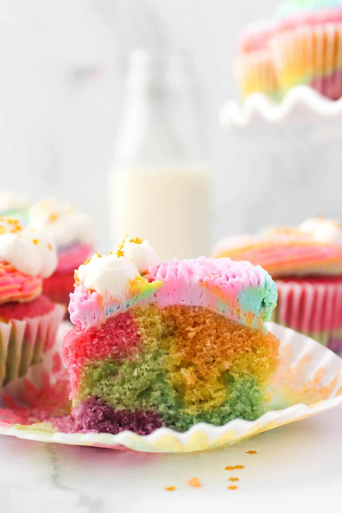Side view of a rainbow cupcake with rainbow frosting cut in half