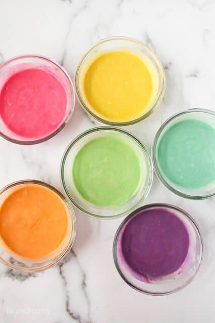 Overhead view of cupcake batter divided into bowl with 6 different colors