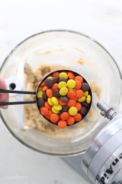 A measuring cup of Reese's pieces over a bowl of cookie dough