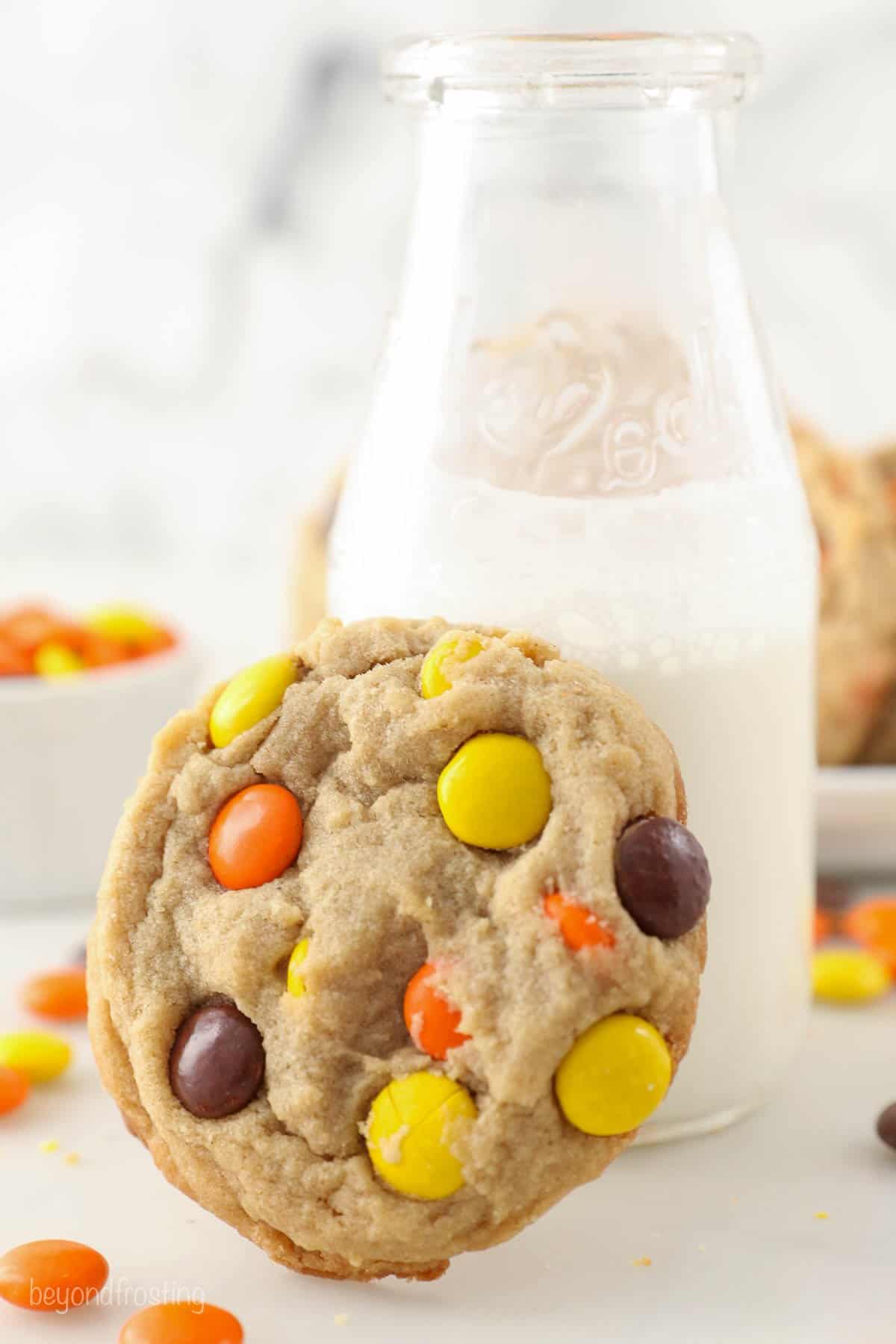 A Reese's peanut butter cookie learning against a glass of milk